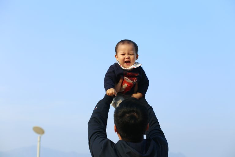 rear-view-man-holding-cheerful-boy-against-blue-sky