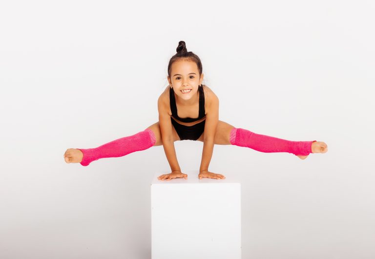 Little gymnast on a large white cube performs sports exercises